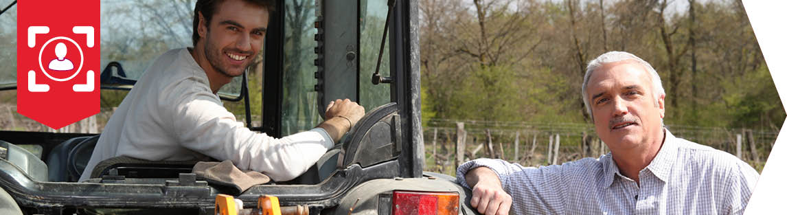 Un jeune repreneur et son cédant l'un à côté de l'autre sur un tracteur rouge.